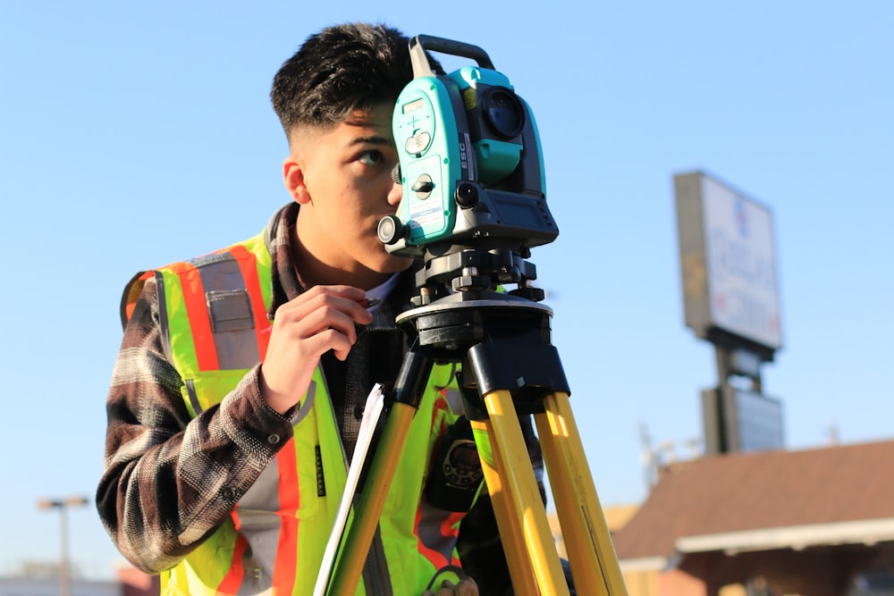 man in gray and orange jacket holding green and black dslr camera during daytime