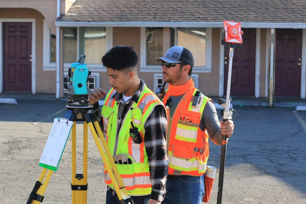 man in orange and yellow jacket holding blue and gray camera