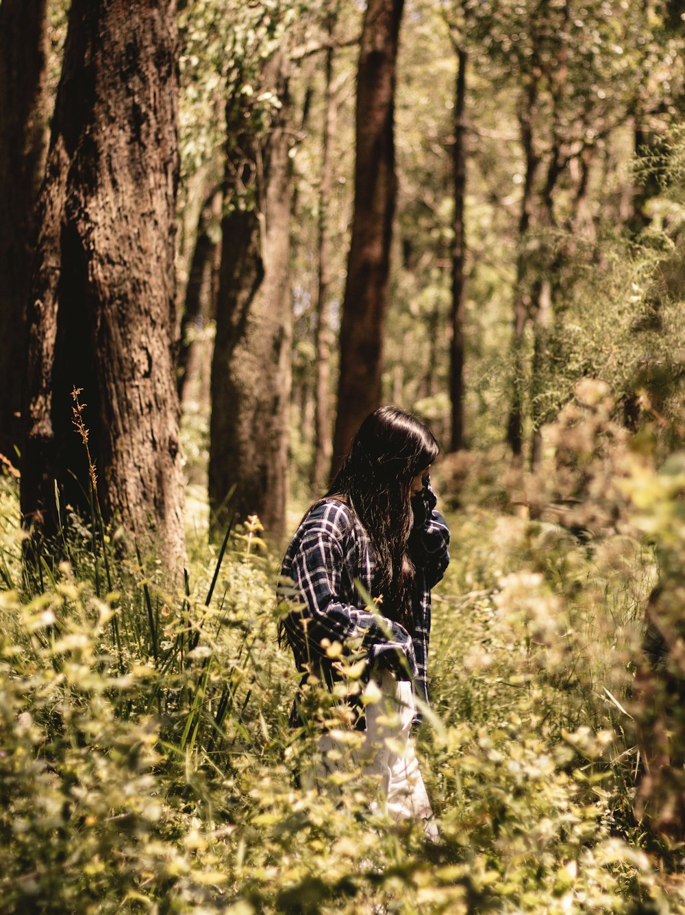 woman in black and white plaid long sleeve shirt standing beside brown tree during daytime