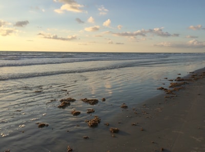 Wide shot of a calm beach at sunset with gentle waves and neutral tones.
