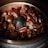 Close-up shot of dark roasted coffee beans inside a metal coffee grinder. The beans are glossy and rich in color, surrounding the central blade of the grinder.