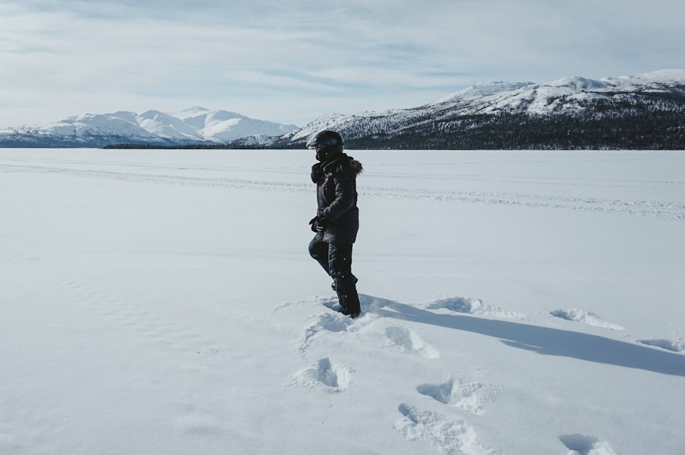 昼間、雪に覆われた地面に立っている黒いジャケットと黒いズボンを着た人