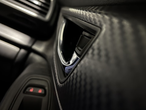 Close-up of a carbon-fiber automotive component with textured weave under bright workshop lighting.