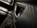 A close-up view of a car interior, focusing on a textured panel with a pattern resembling carbon fiber. The image features part of a car door with a chrome-accented handle and nearby buttons, possibly for window or lock controls. The overall look is sleek and modern.