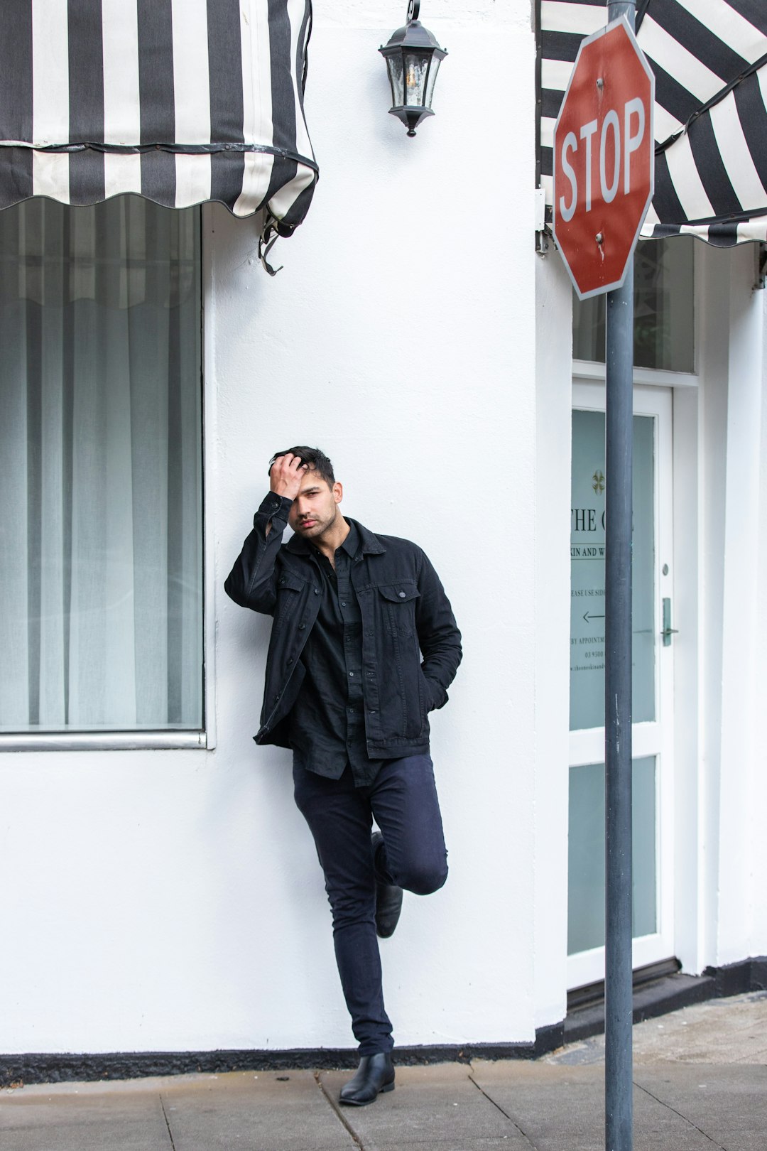 man in black leather jacket and blue denim jeans standing near white wall