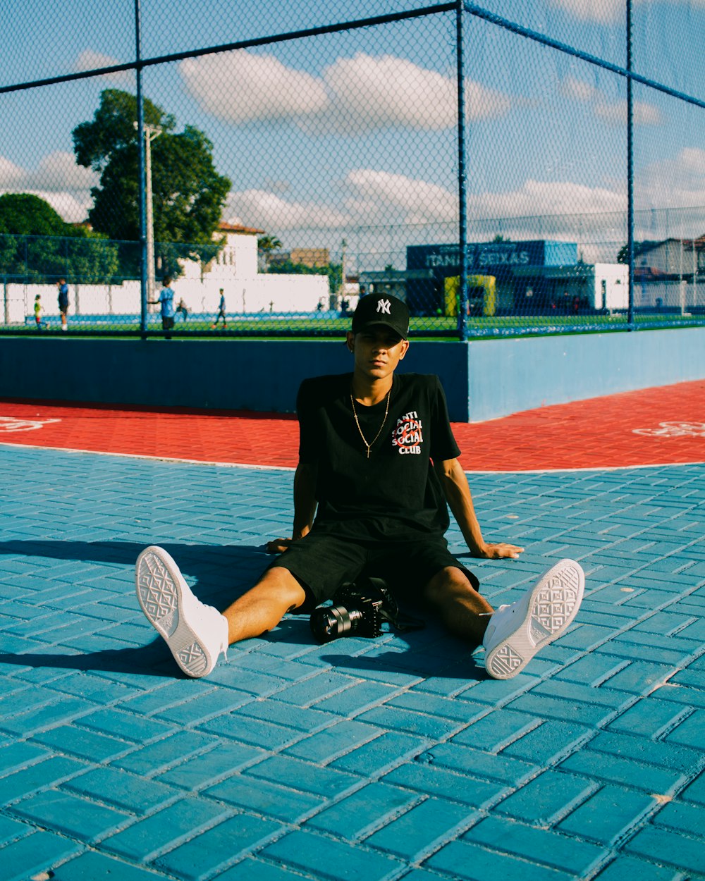 man in black polo shirt and black pants sitting on basketball court during daytime