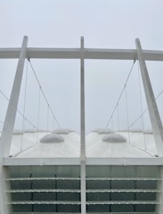 A modern architectural structure with a series of large, white, tent-like canopies supported by steel cables and beams. The canopies have dome-shaped tops and the structure appears minimalistic and geometric.