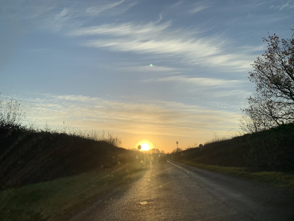 Graue Asphaltstraße zwischen grünem Grasfeld bei Sonnenuntergang