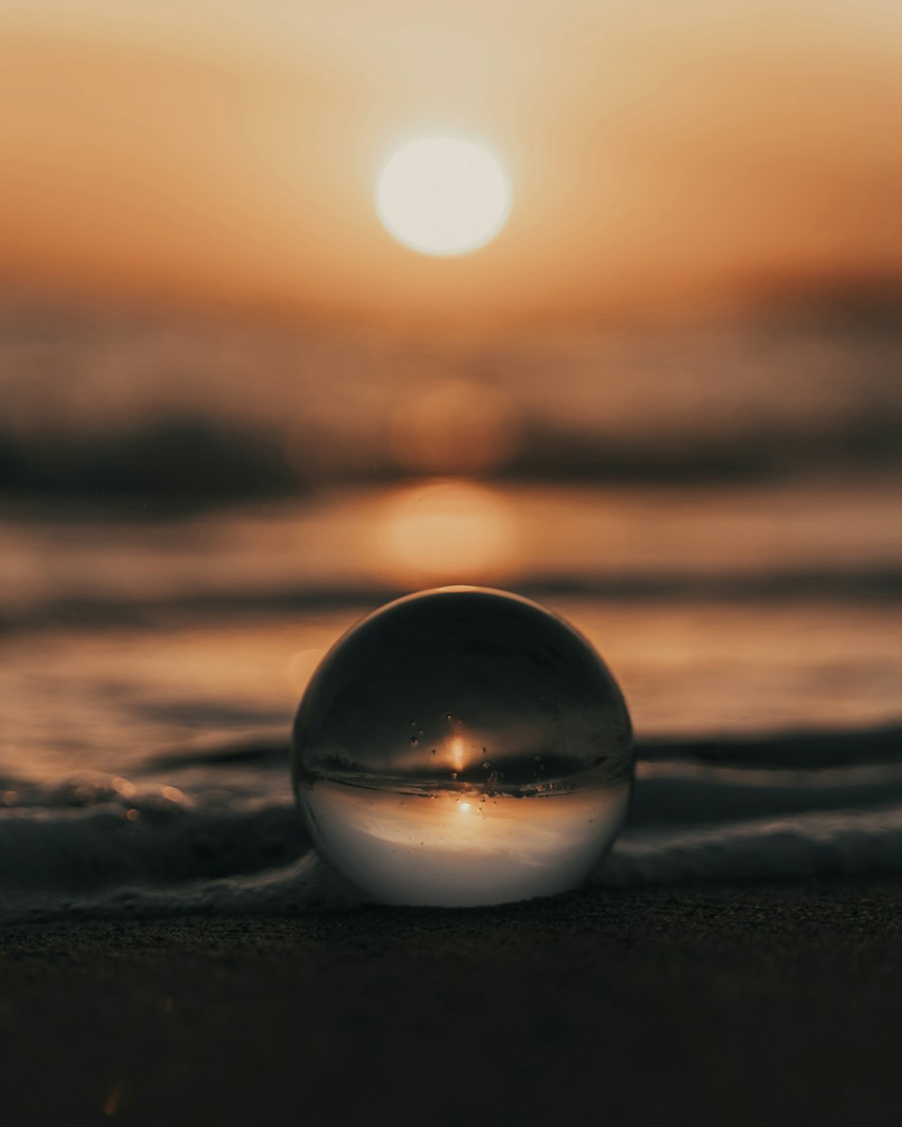 Boule de verre clair sur sable brun au coucher du soleil