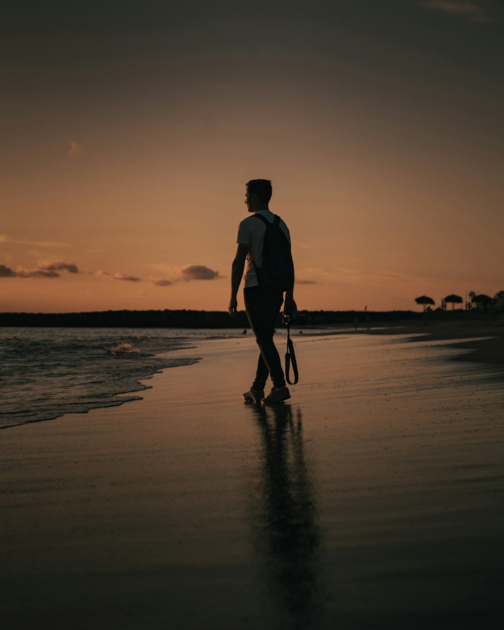 Silhouette eines Mannes, der während des Sonnenuntergangs am Strand spazieren geht