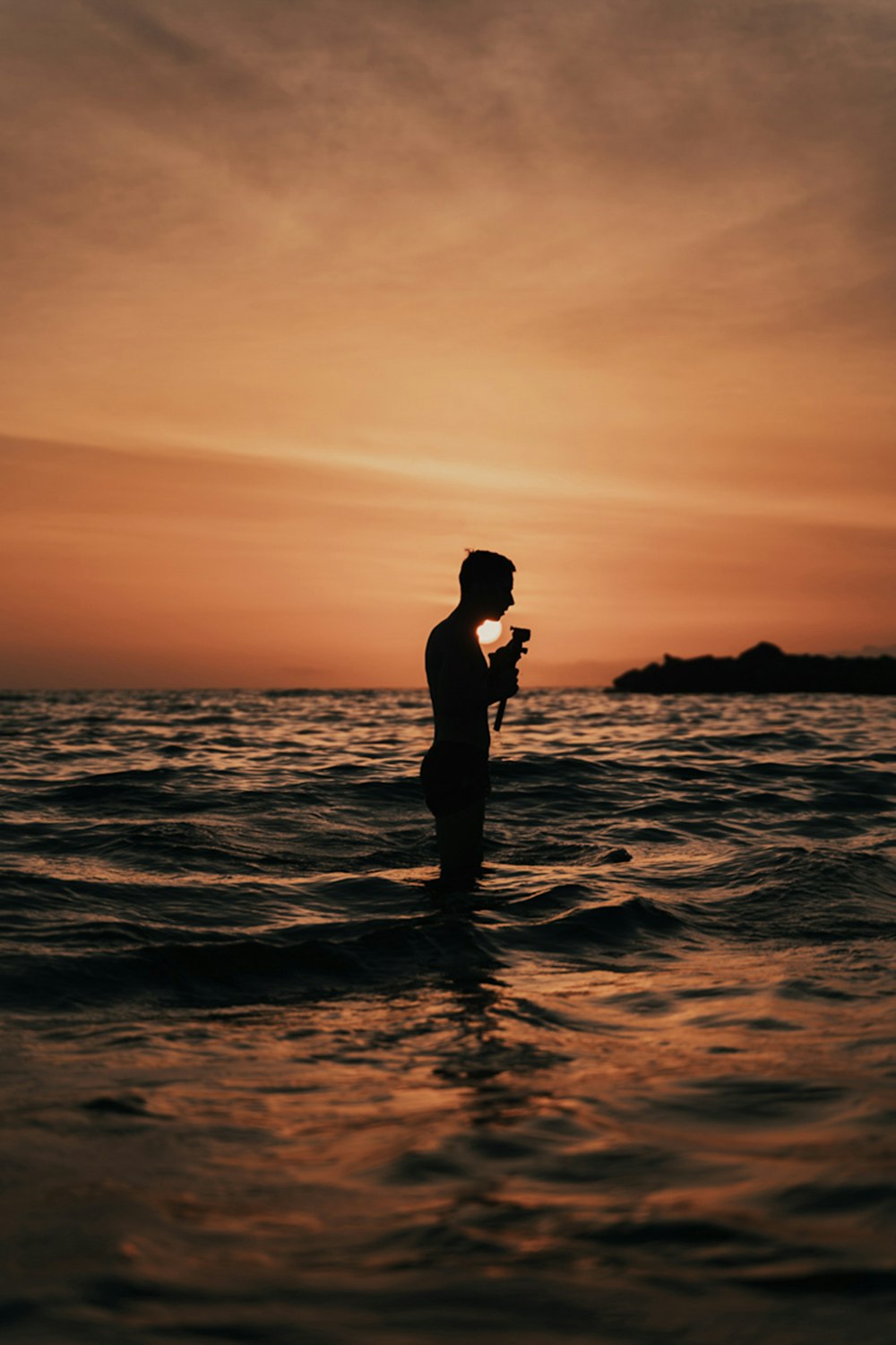 silhouette of man standing on sea shore during sunset