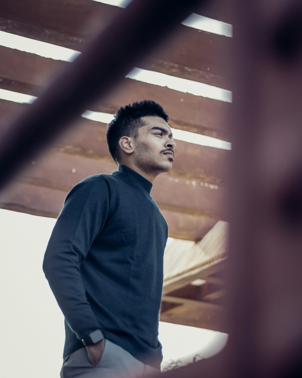 man in blue long sleeve shirt standing near brown wooden wall