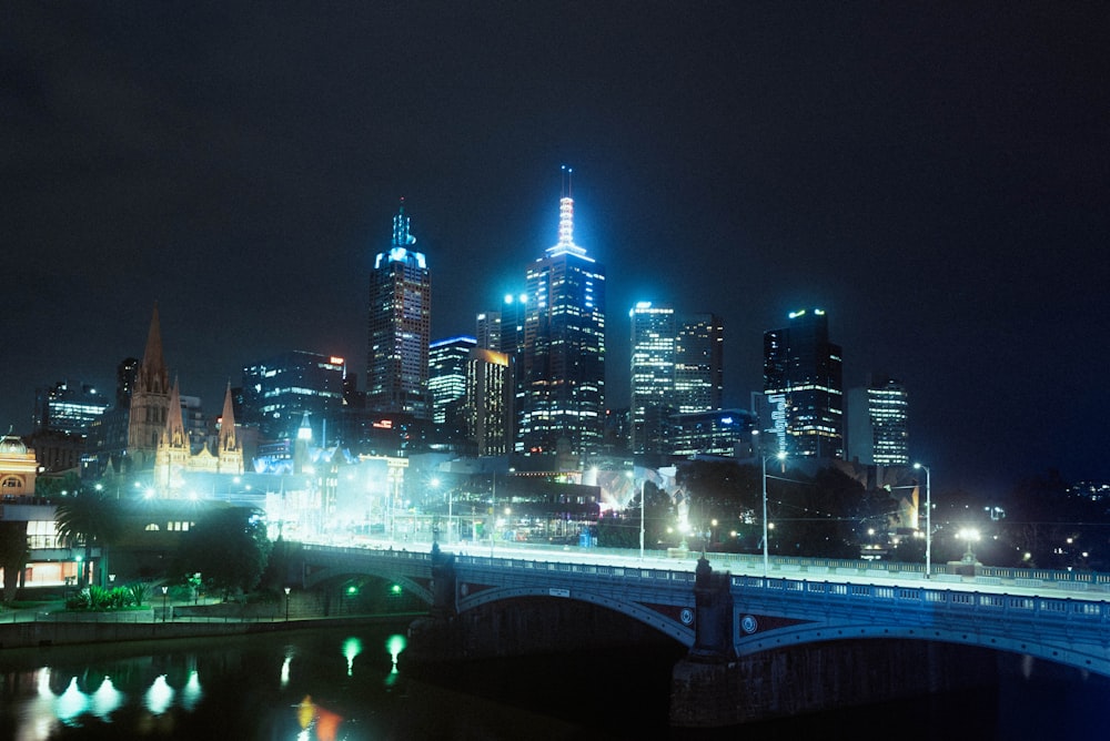 lighted bridge over water near city buildings during night time