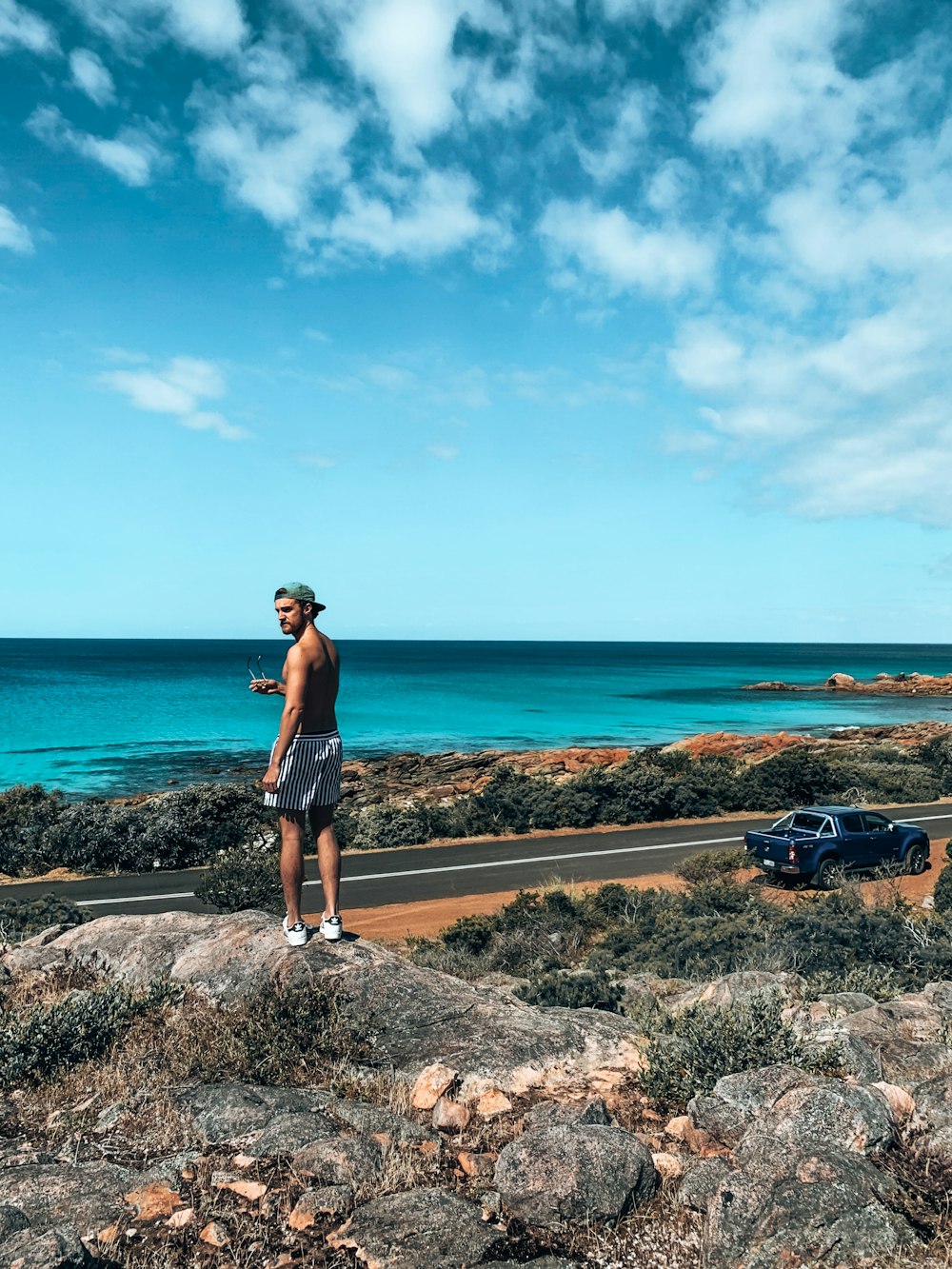 woman in black tank top and white shorts standing on brown rock formation near body of near near near near