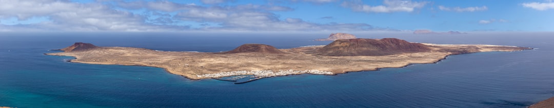 brown and green mountain beside blue sea under blue sky during daytime