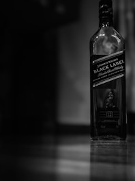 A dramatic studio photo of a rare aged whisky bottle with warm golden highlights on matte black background.