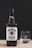 A bottle of Jim Beam Kentucky Straight Bourbon Whiskey with a glass beside it on a wooden surface. The bottle has a black cap and a white label with red and black text. The glass is clear with the brand logo etched on it, and the background is a plain black color.