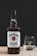 A bottle of Jim Beam Kentucky Straight Bourbon Whiskey with a glass beside it on a wooden surface. The bottle has a black cap and a white label with red and black text. The glass is clear with the brand logo etched on it, and the background is a plain black color.