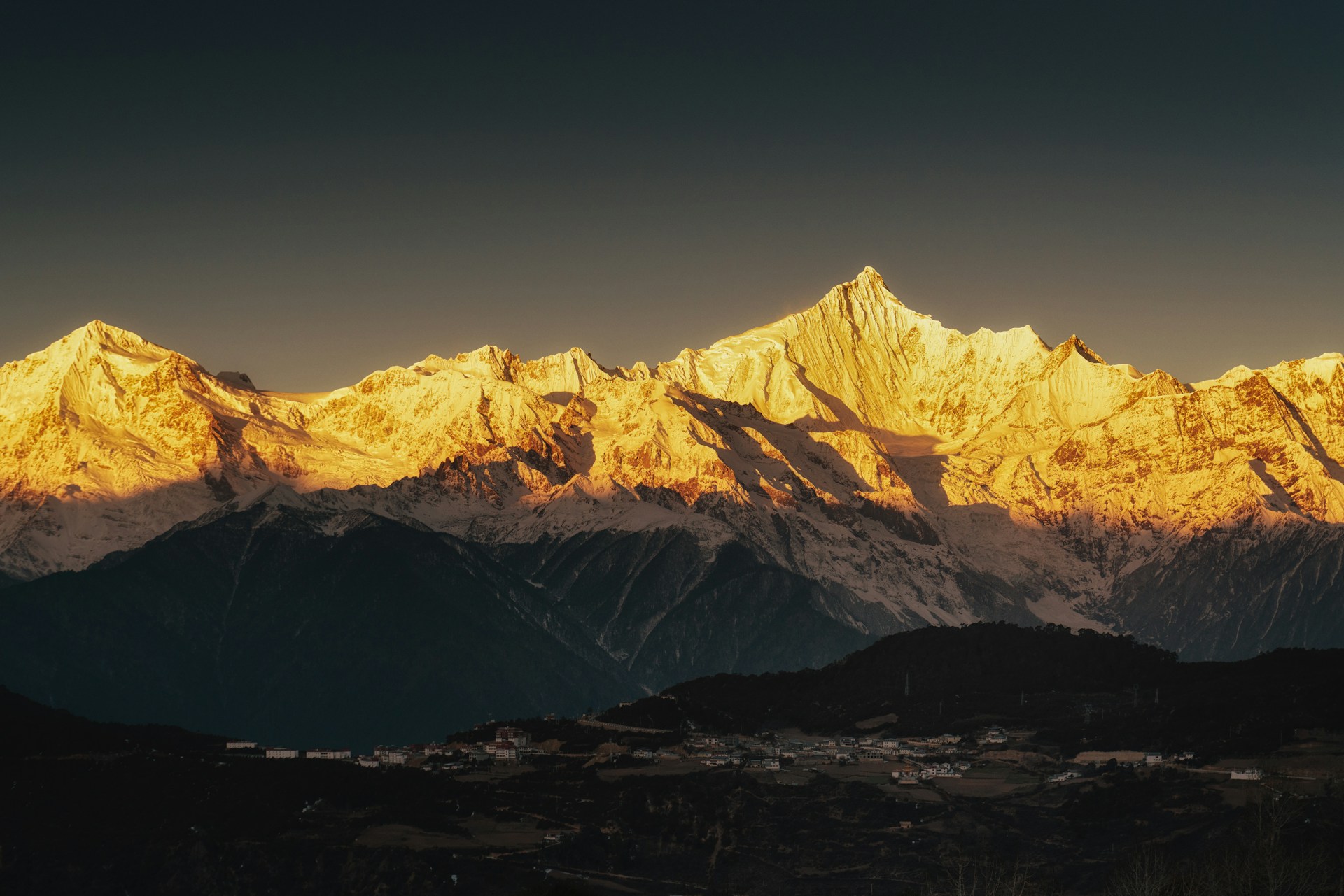 A breathtaking morning view of K2's rugged peak illuminated by golden sunlight, with trekkers starting their journey in the foreground.