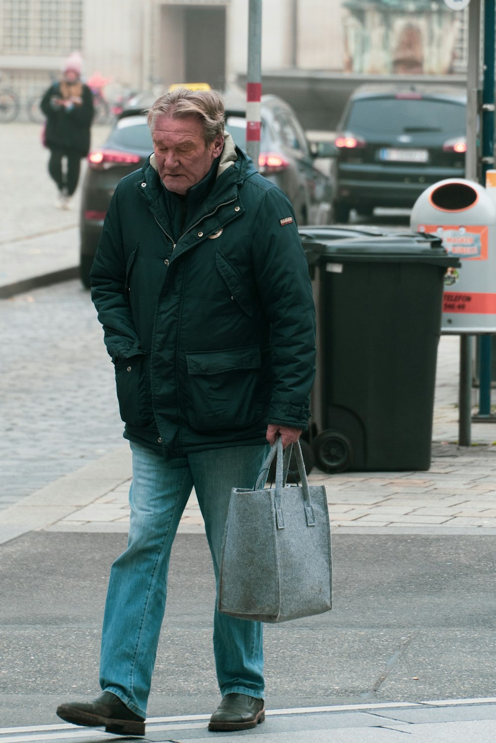 man in black jacket and blue denim jeans holding gray handbag