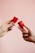 Two hands are holding red menstrual cups against a soft pink background. The hands are positioned to face each other, with each hand holding a single cup between the thumb and fingers.