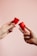 Two hands are holding red menstrual cups against a soft pink background. The hands are positioned to face each other, with each hand holding a single cup between the thumb and fingers.