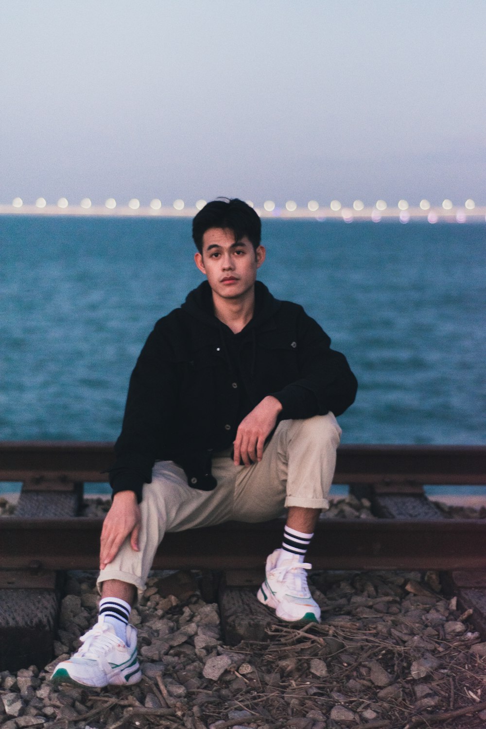 man in black jacket and white pants sitting on brown wooden bench