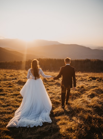 man and woman in wedding dress walking on brown grass field during daytime
