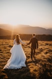 man and woman in wedding dress walking on brown grass field during daytime