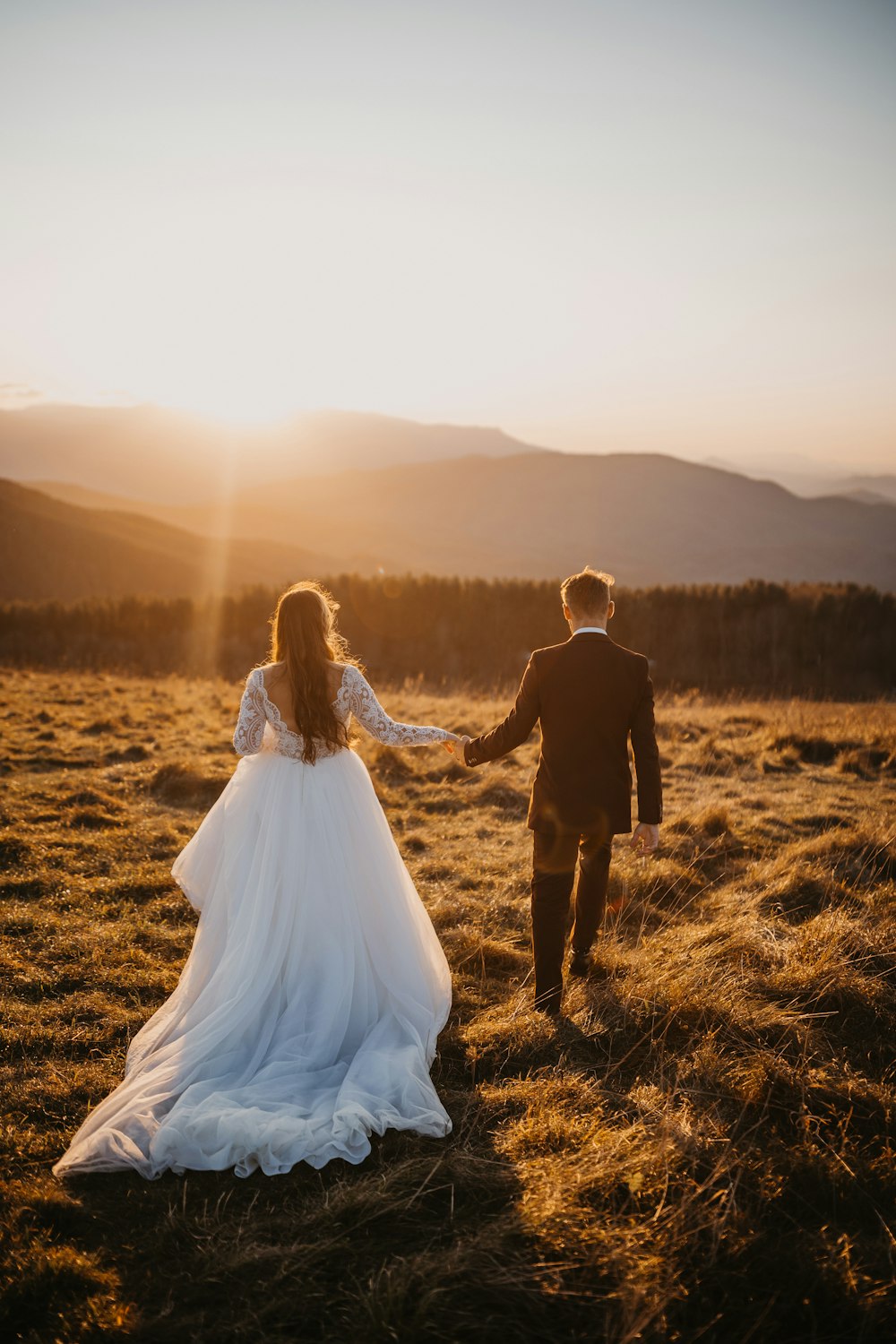 uomo e donna in abito da sposa che camminano sul campo di erba marrone durante il giorno