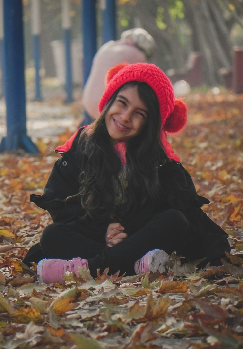 woman in black jacket and red knit cap sitting on dried leaves