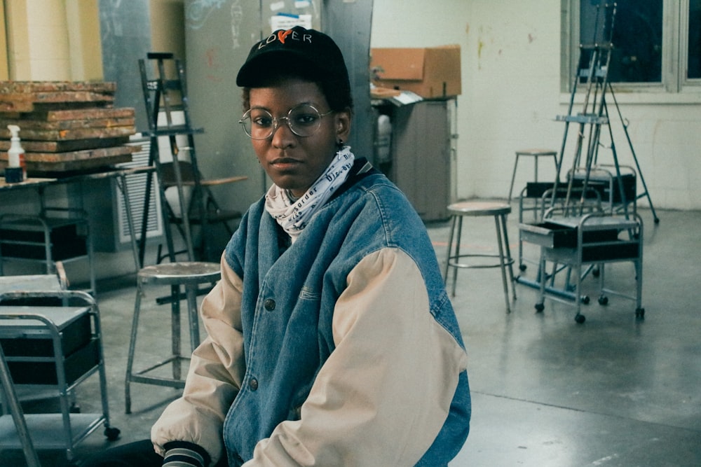 man in blue denim jacket and black cap sitting on chair