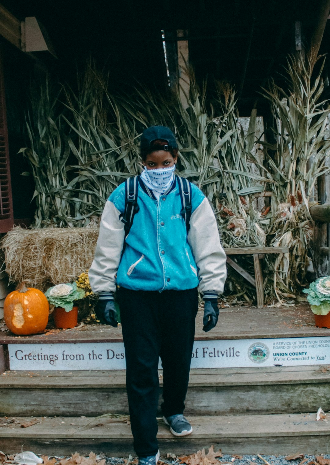 man in blue and white jacket standing beside orange pumpkins during daytime