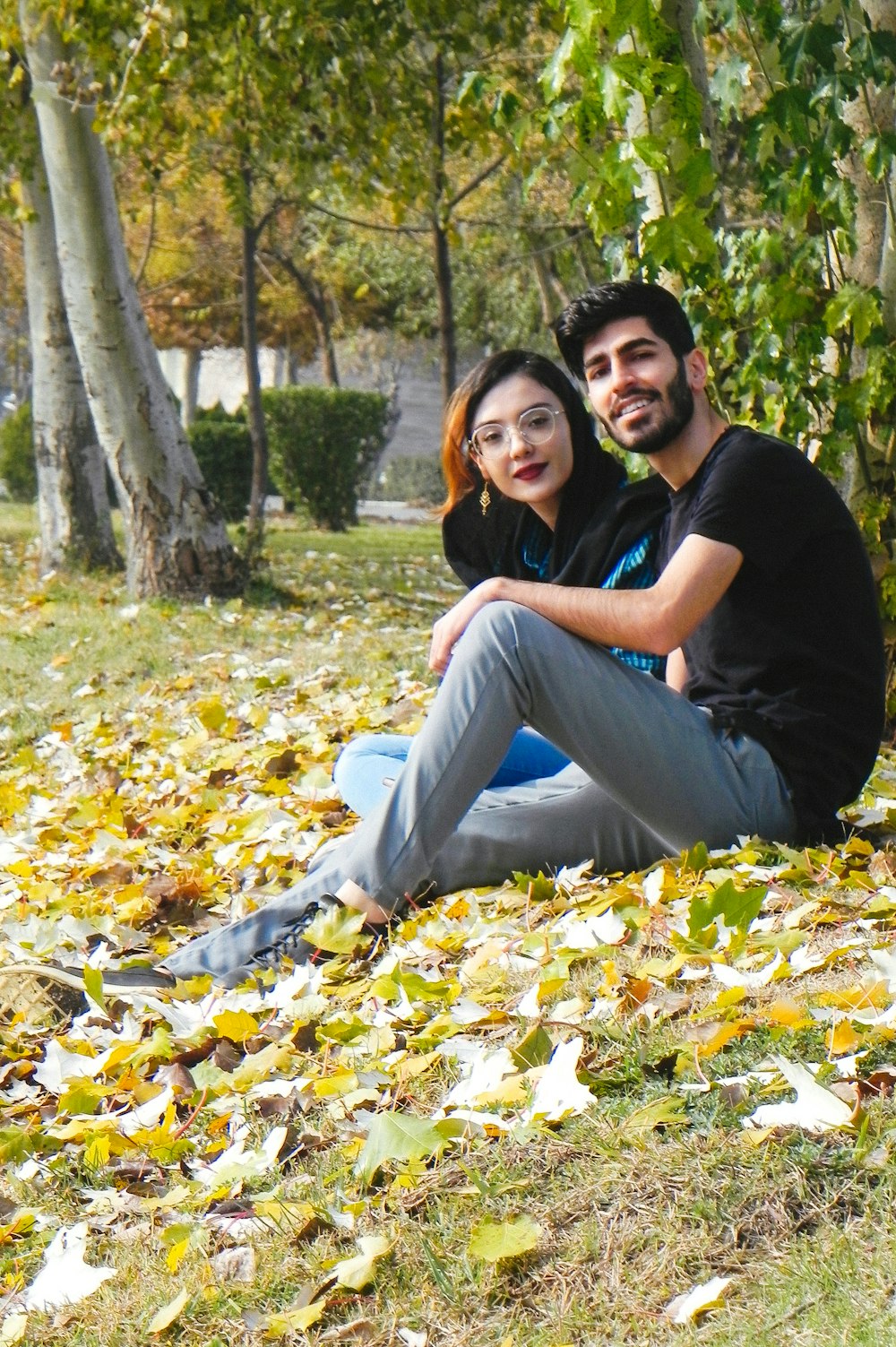 man in black t-shirt and blue denim jeans sitting on ground with dried leaves