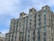 A multi-story hotel building with a modern architectural design featuring numerous windows and balconies. The structure is made of gray stone, and the word 'HOTEL' is prominently displayed at the top. The sky is partly cloudy, creating a peaceful atmosphere.