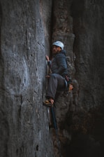 man in black jacket and white cap climbing on gray rock