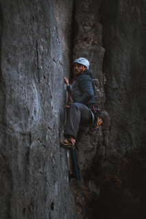 man in black jacket and white cap climbing on gray rock