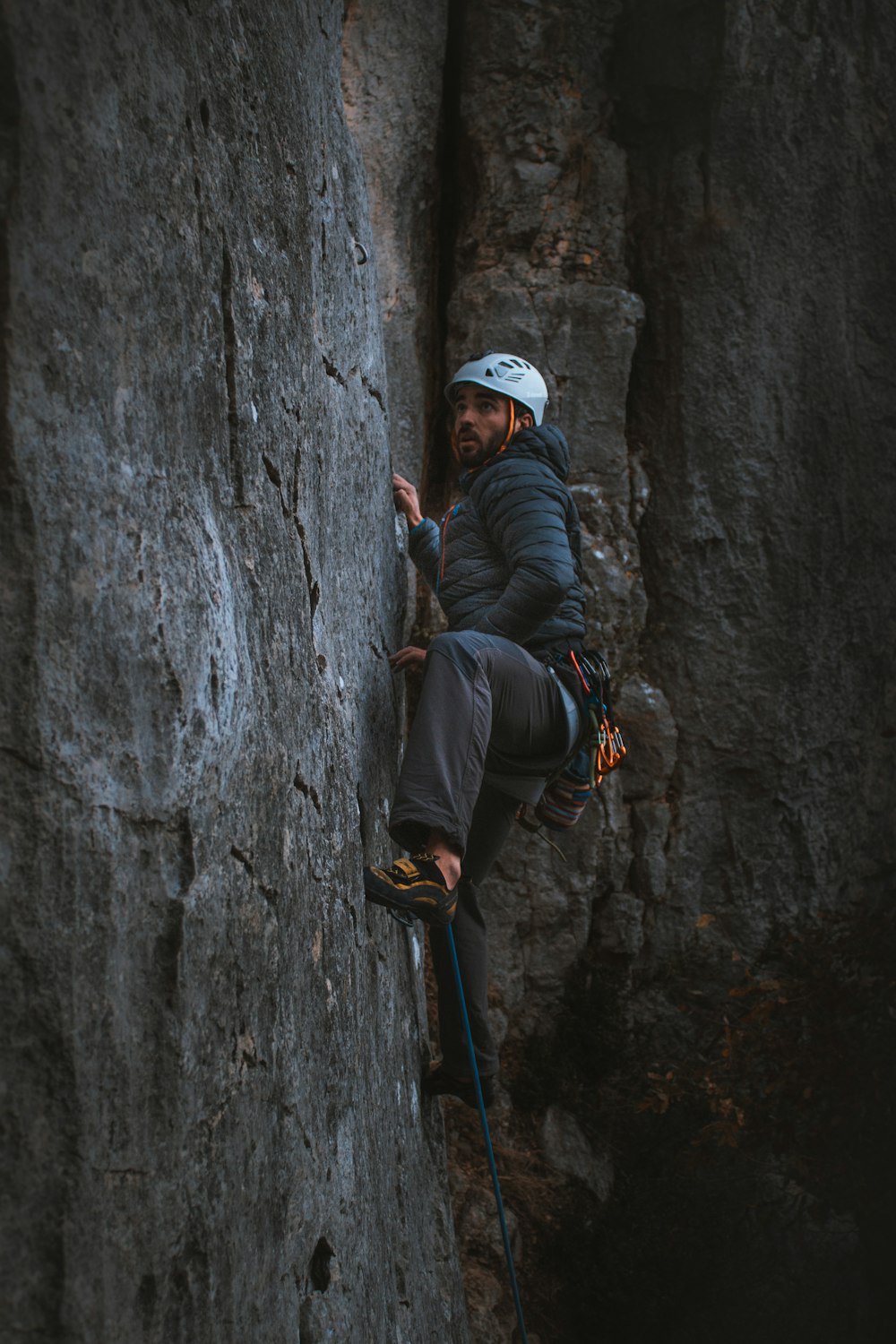 Hombre con chaqueta negra y gorra blanca escalando en roca gris