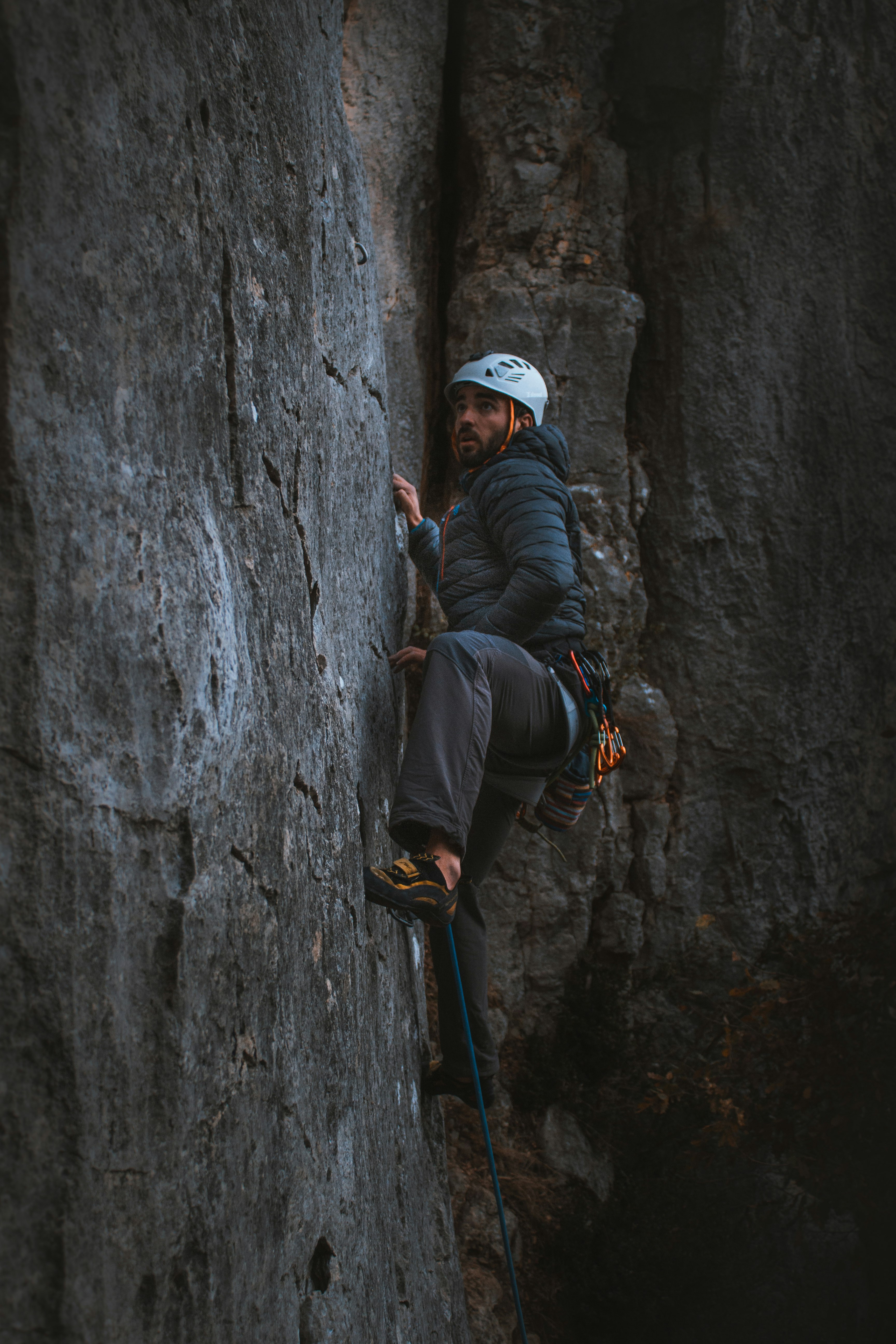 man in black jacket and white cap climbing on gray rock