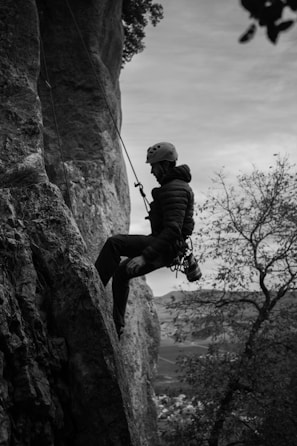 grayscale photo of man climbing on rock