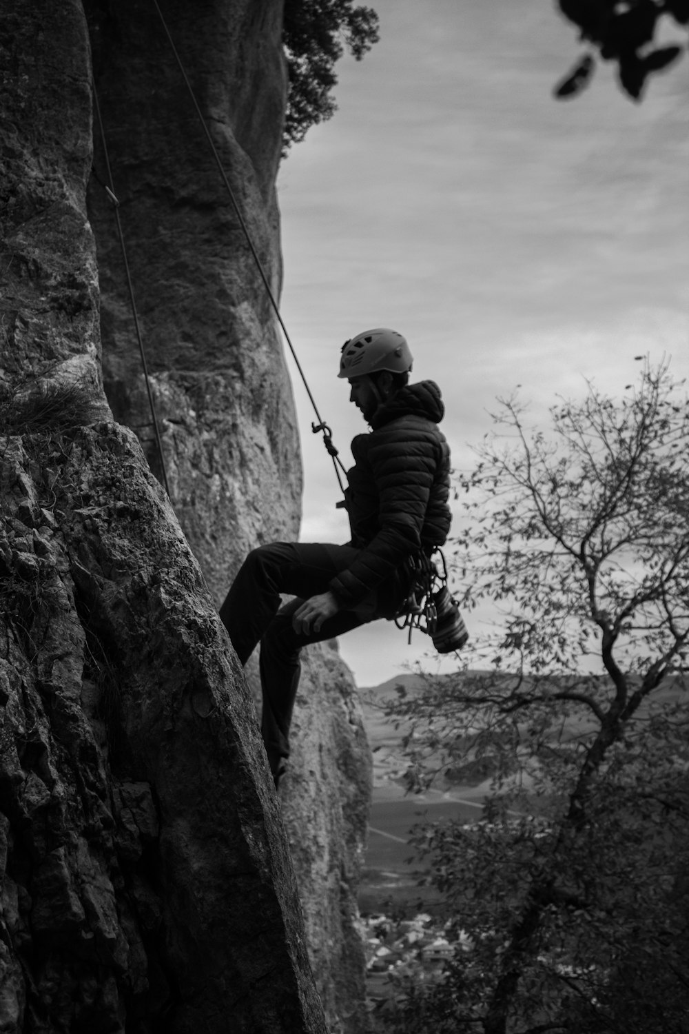 grayscale photo of man climbing on rock