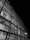 A detailed view of a modern architectural structure with a glass facade showcasing intricate steel beams and structural components. The image is in black and white, highlighting the contrast between the illuminated interior and the dark exterior.