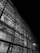 A detailed view of a modern architectural structure with a glass facade showcasing intricate steel beams and structural components. The image is in black and white, highlighting the contrast between the illuminated interior and the dark exterior.
