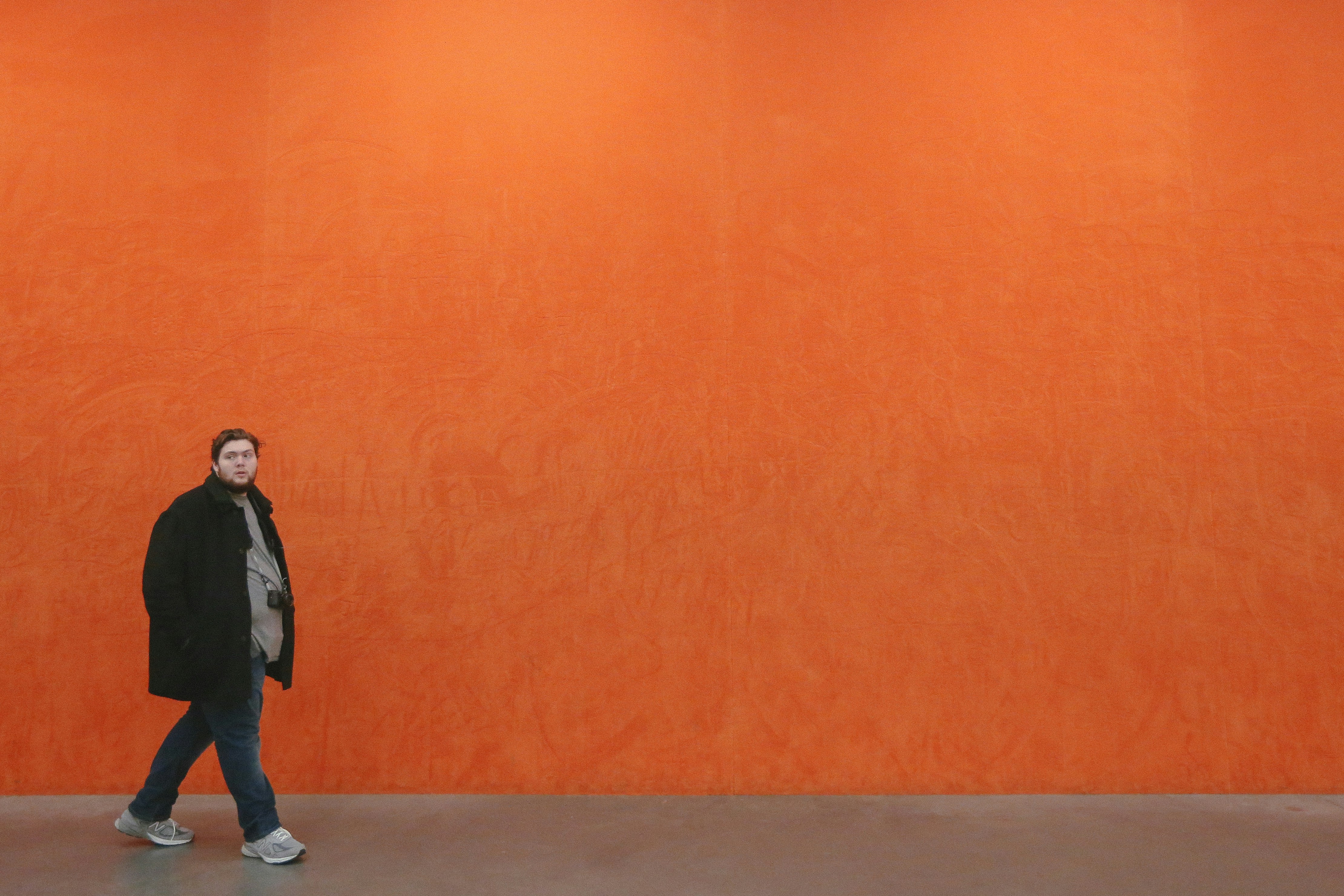 man in black jacket and blue denim jeans standing beside orange wall