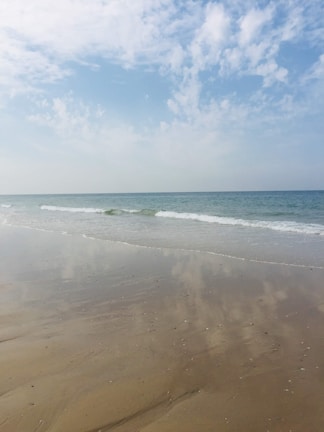 Sandy beach with gentle waves and a peaceful neighborhood street.
