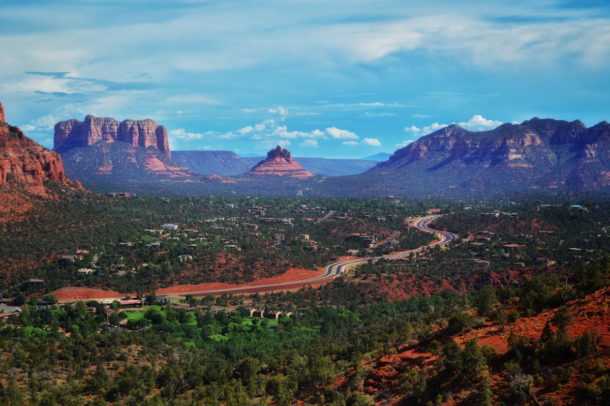 A road winding through Sedona among red rock buttes and green scrub