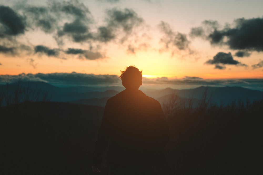 silhueta do homem de pé na montanha durante o pôr do sol