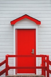 Freshly painted house exterior featuring a bold red front door and crisp white siding under a clear sky.