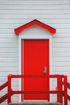 A bright red front door contrasting beautifully with soft white exterior walls.