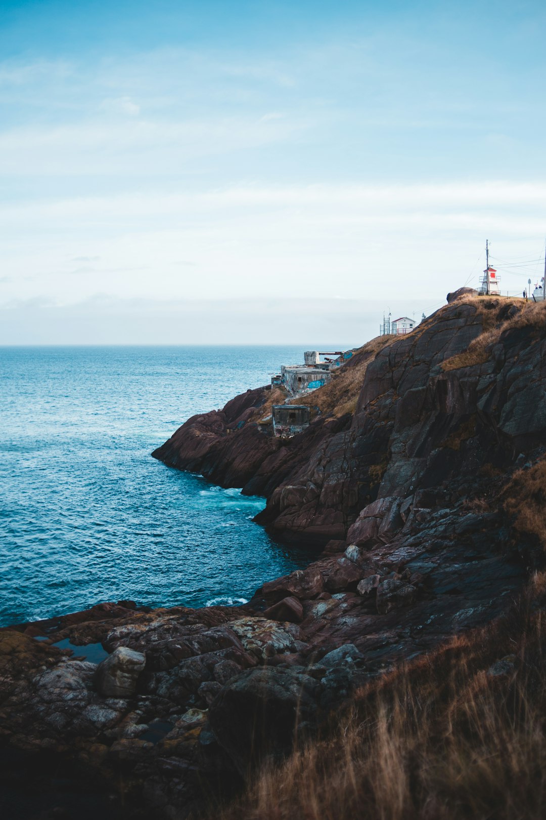 white and red lighthouse on brown rock formation near body of water during daytime